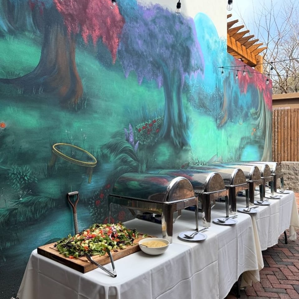 Buffet tables with chafing dishes and salad set against a vibrant, whimsical mural outdoors.