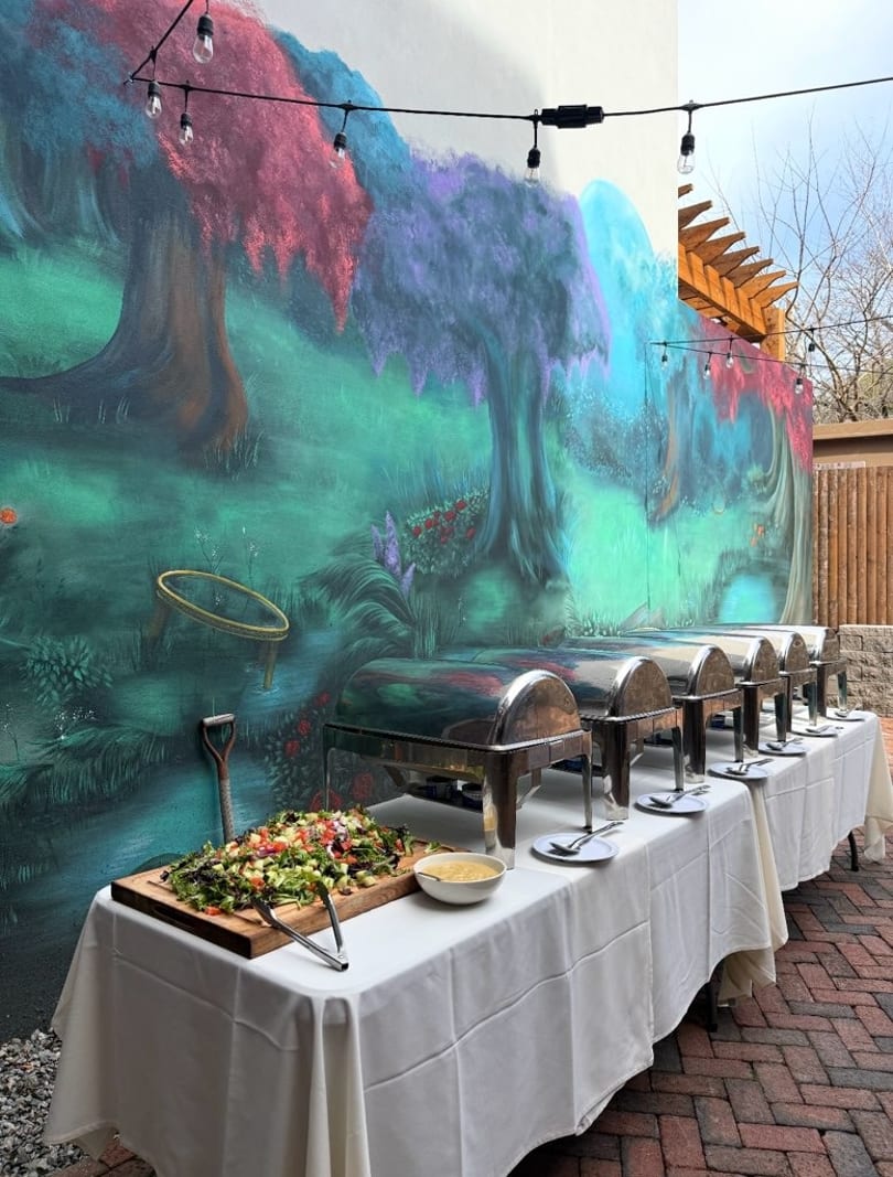 Buffet tables with chafing dishes and salad set against a vibrant, whimsical mural outdoors.